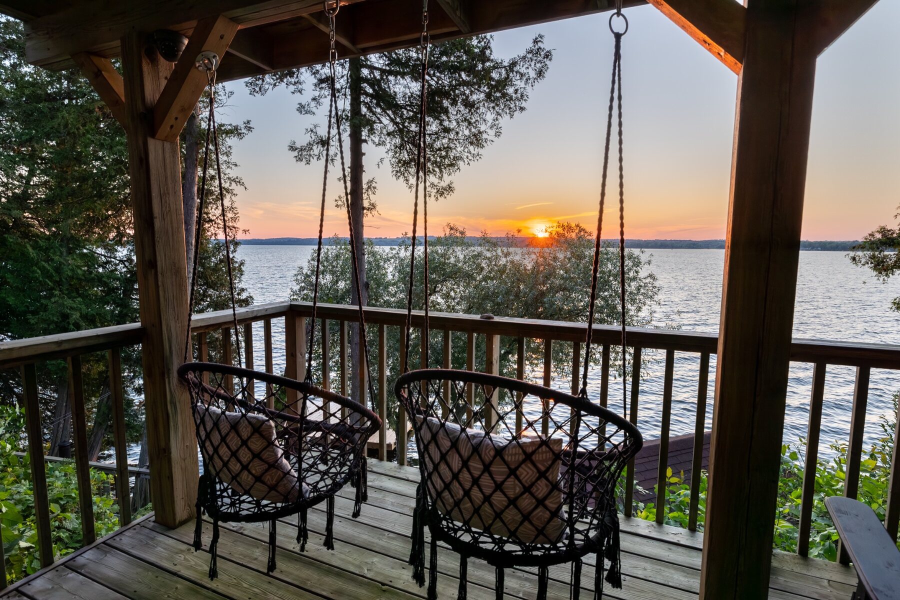Hanging chairs on a deck facing a sunset over Rice Lake